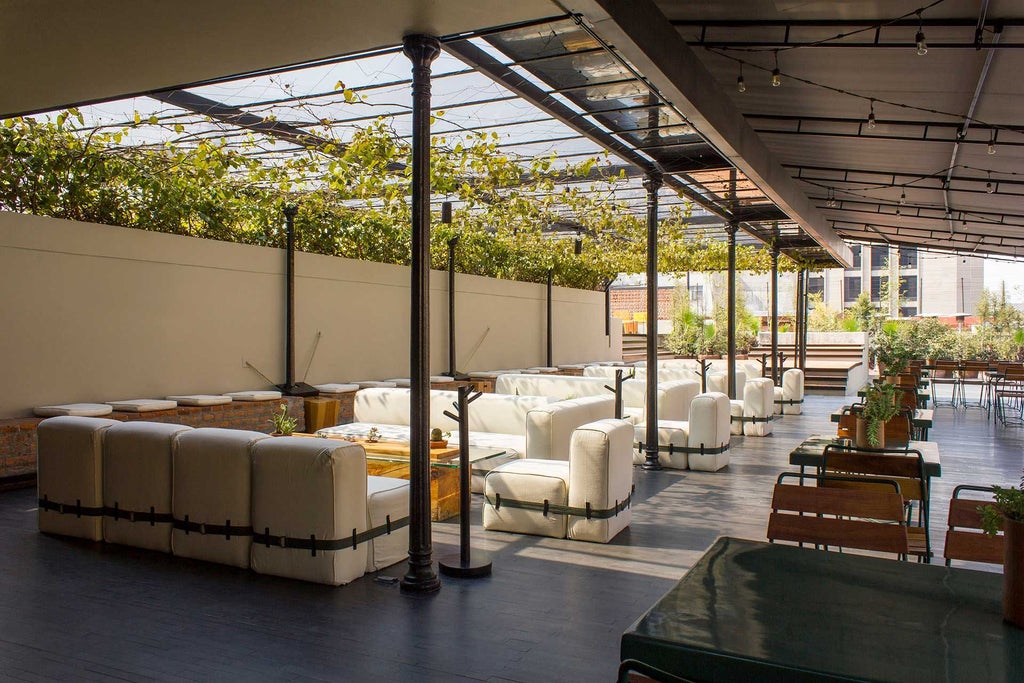 Elegant colonial-style hotel lobby with high ceilings, arched windows, modernist furniture, and vibrant Mexican textiles in warm terracotta tones