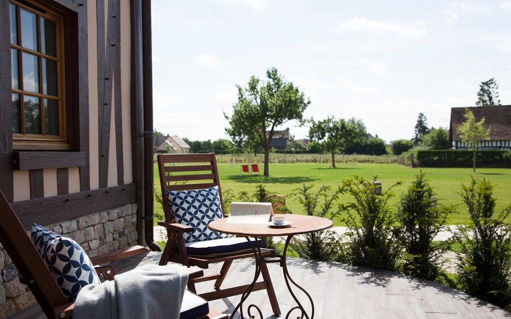 Elegant French classic hotel room with soft beige linens, antique wooden furniture, large windows overlooking manicured countryside gardens at Manoir de Surville