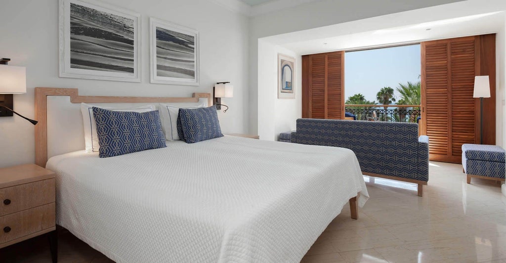 Luxurious deluxe sea view room at coastal Cyprus hotel, featuring elegant white decor, plush king bed, and panoramic azure Mediterranean vista