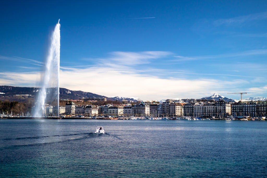 Aerial view of Geneva's iconic Jet d'Eau fountain spraying above Lake Geneva, with snow-capped Alps and elegant waterfront buildings