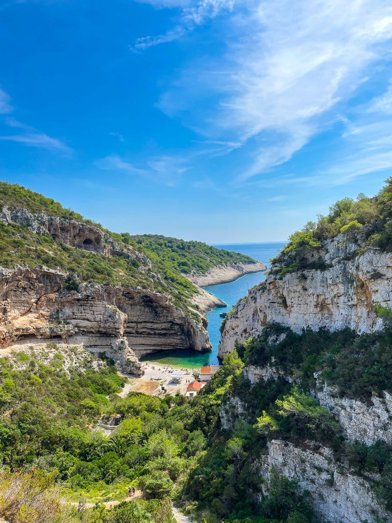 Luxury white speedboat anchored in crystal-clear turquoise waters near Croatian coastline with rugged cliffs and azure sky above