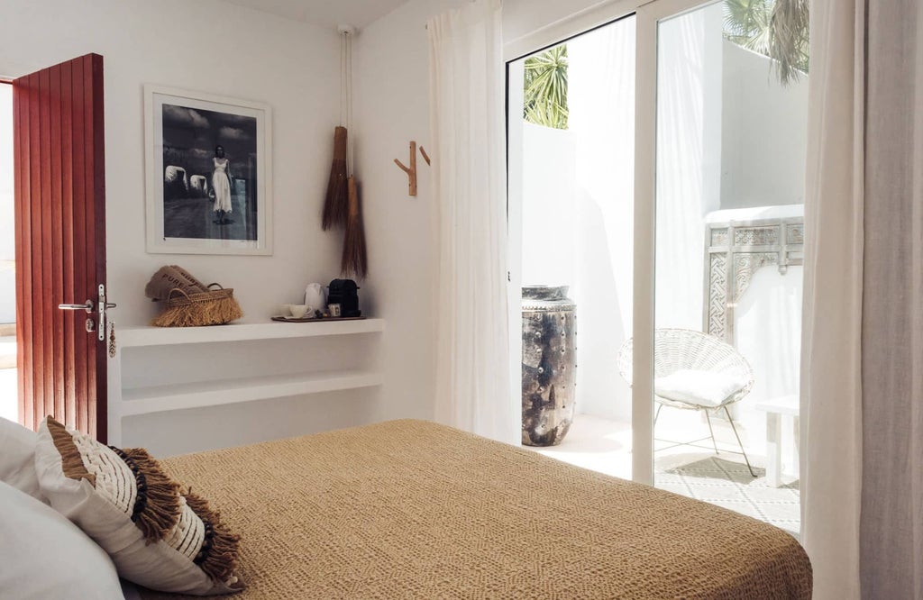 Minimalist white bedroom with sleek wooden accents, crisp linens, and large window offering panoramic view of Scenset landscape at Hotel Pure House Ibiza