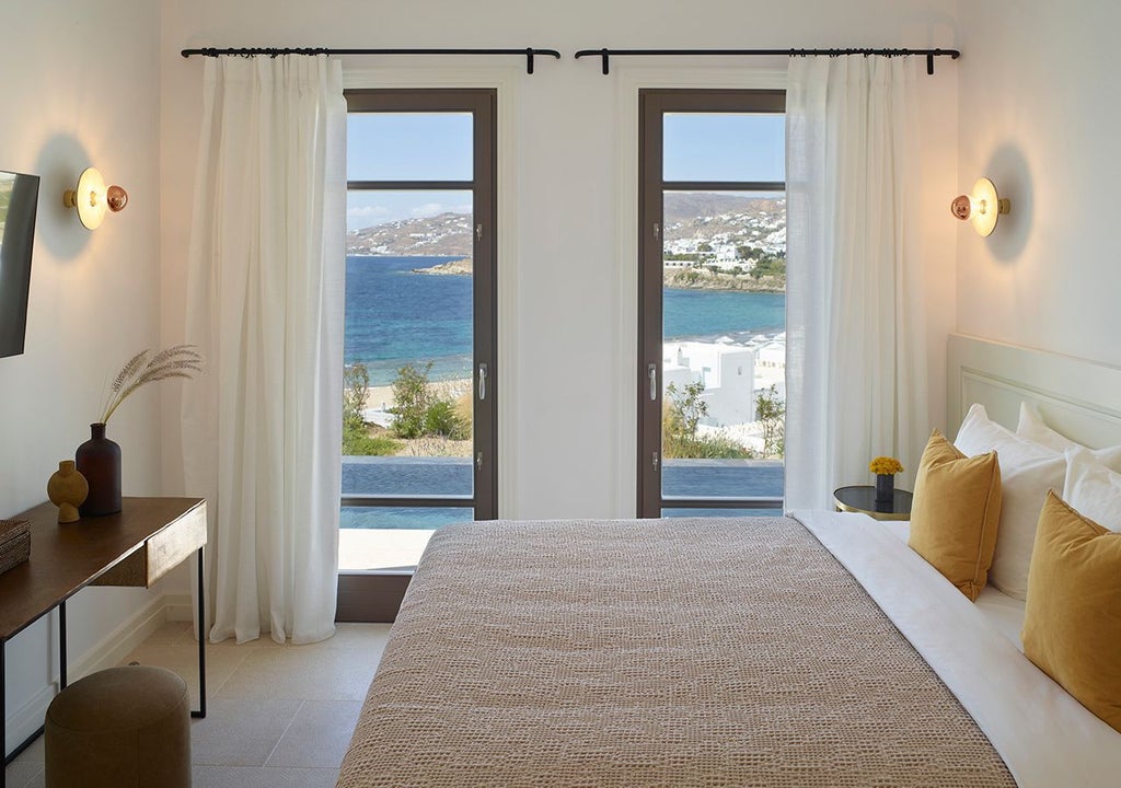 Luxurious two-bedroom Grecian villa with private heated pool overlooking azure Mykonos seas, featuring modern white architecture and stunning coastal panorama