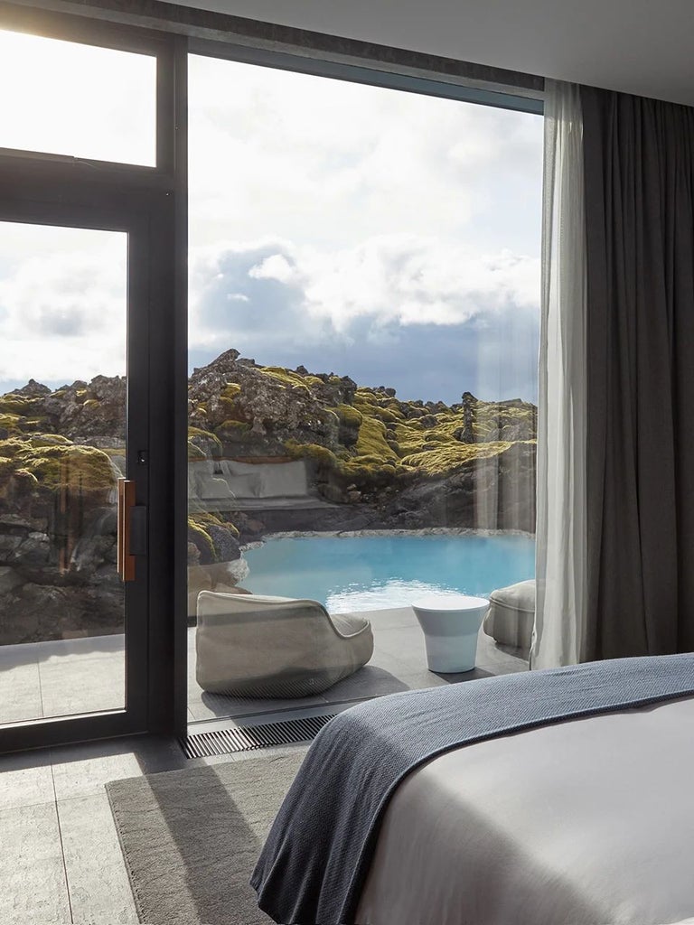 Luxurious minimalist Icelandic hotel room with floor-to-ceiling windows overlooking volcanic landscape, modern Nordic design, and serene lagoon view.