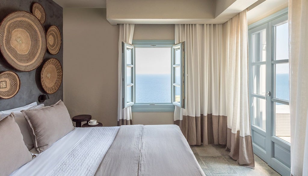 Minimalist white bedroom with panoramic Aegean Sea view, elegant Cycladic design, clean lines, and natural light streaming through large windows at Verina Astra hotel.