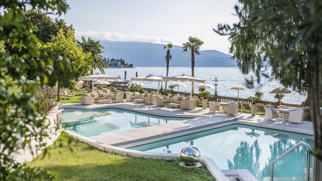 Historic luxury hotel with ornate pink façade overlooking Lake Garda, featuring elegant palm trees and classical Italian architecture