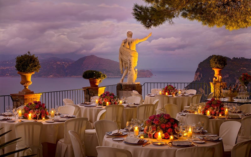 Cliffside luxury hotel overlooking Bay of Naples, featuring a white stone terrace with infinity pool and Mediterranean gardens