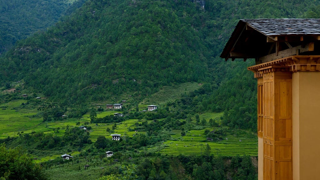 Elegant hotel room with panoramic Himalayan valley views, traditional Bhutanese wooden accents, plush white bedding, and minimalist luxury design