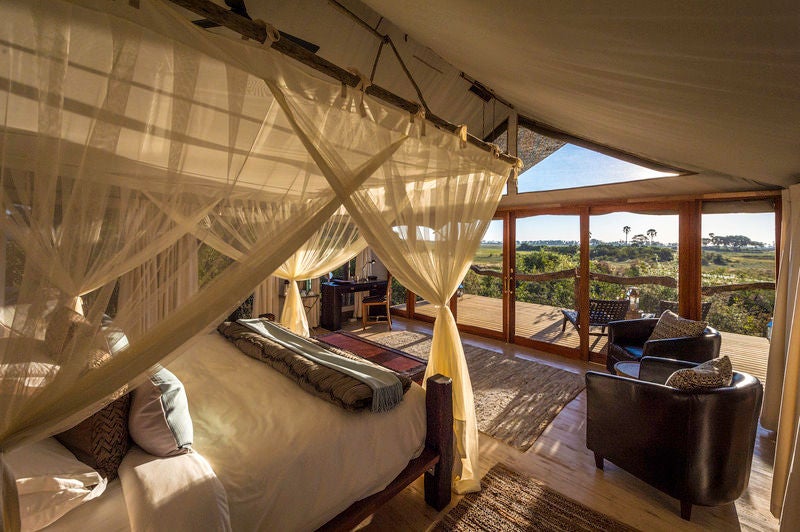 Elevated luxury safari tent overlooking a vast grassland, with wooden deck, private plunge pool and contemporary outdoor furniture