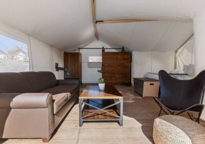 Luxurious glamping suite with canvas walls, rustic wooden bed, and panoramic nature views of Zion's dramatic landscape through large tent windows.