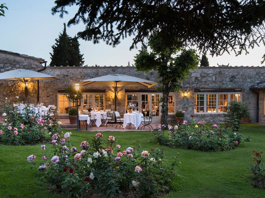 Elegant Tuscan hotel complex with stone buildings, terracotta roofs, and manicured gardens nestled among rolling vineyard hillsides