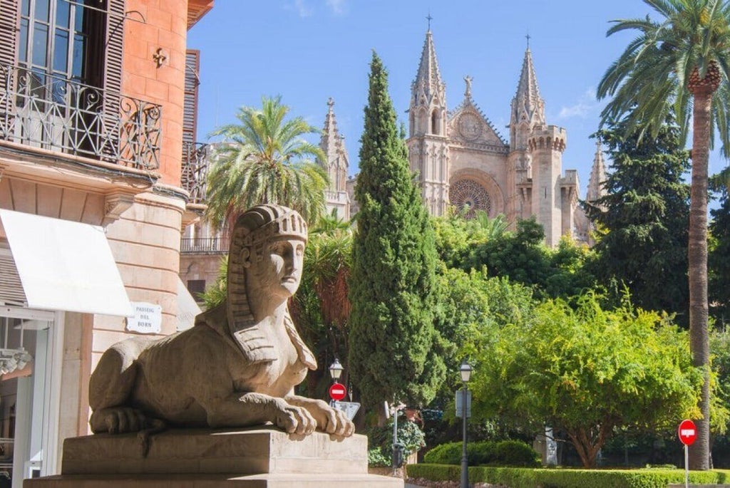 Elegant beige stone facade of boutique luxury hotel with ornate balconies, set against blue sky in historic Spanish architectural style in Palma de Mallorca