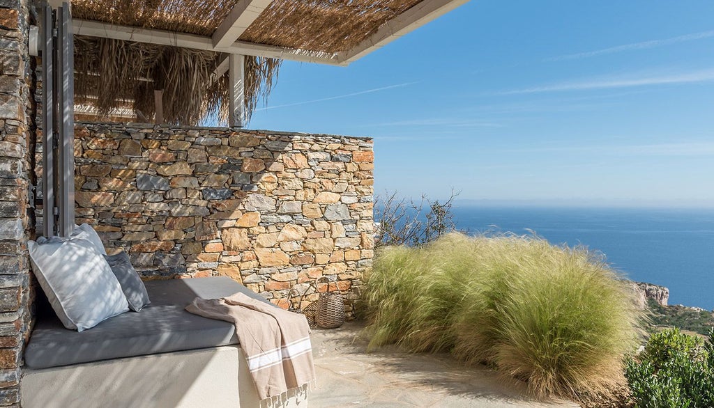 Minimalist white suite with panoramic Aegean Sea view, elegant blue-gray furnishings, sleek design, and private terrace overlooking scenic Greek island landscape.