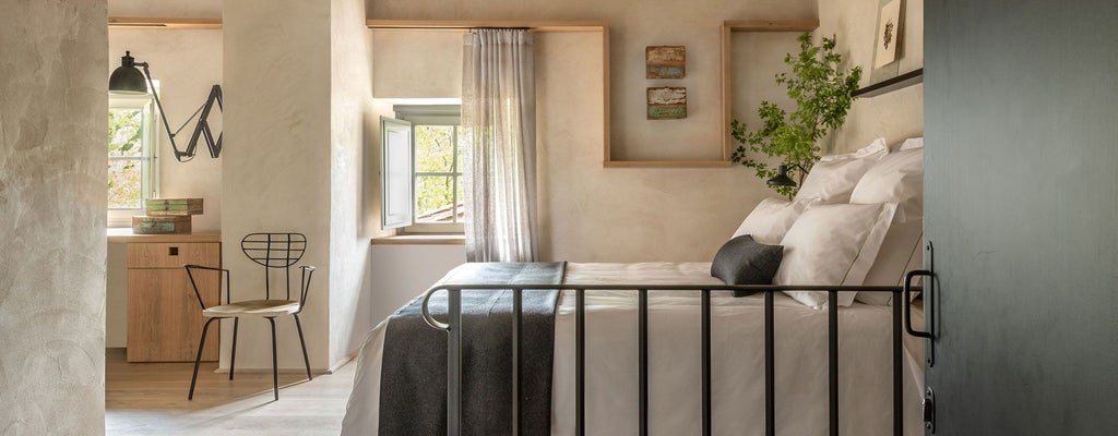 Elegant superior room at Badia di Pomaio, showcasing rustic Tuscan design with wooden floors, plush bedding, and soft natural light streaming through large windows.