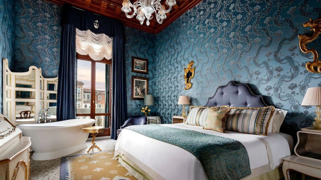 Opulent hotel suite with ornate Venetian mirrors, crystal chandeliers, and antique furniture overlooking the Grand Canal in Venice