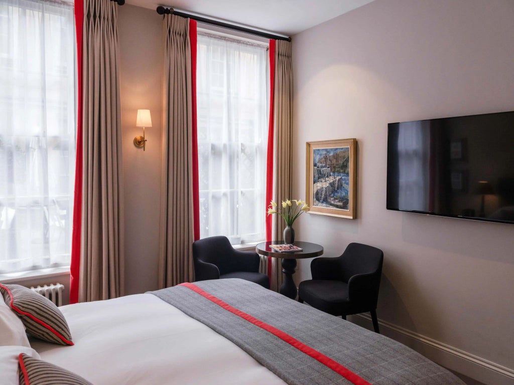 Elegant high-ceiling classic hotel room with antique mahogany furnishings, soft neutral color palette, and refined architectural details from historic United Kingdom property