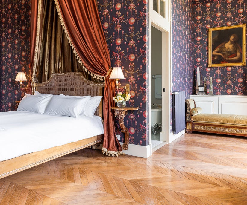 Elegant king room with French doors opening to manicured gardens, featuring ornate moldings, chandeliers and period furnishings in creamy tones