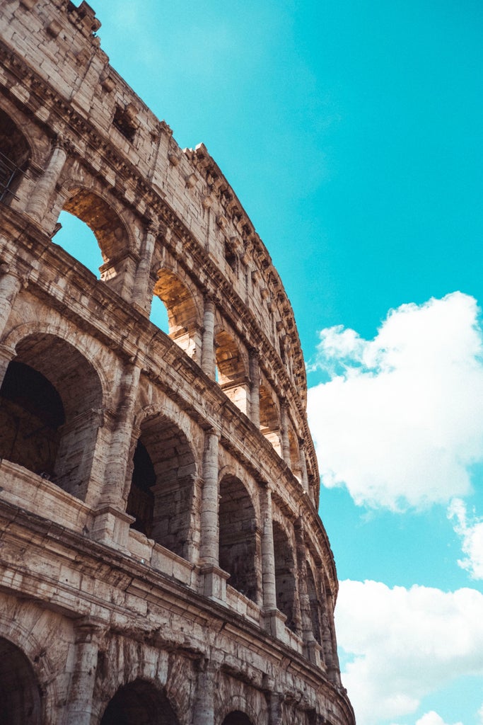 Historic Colosseum in Rome illuminated at dusk, with dramatic stone arches and columns bathed in warm golden lighting against a deep blue sky