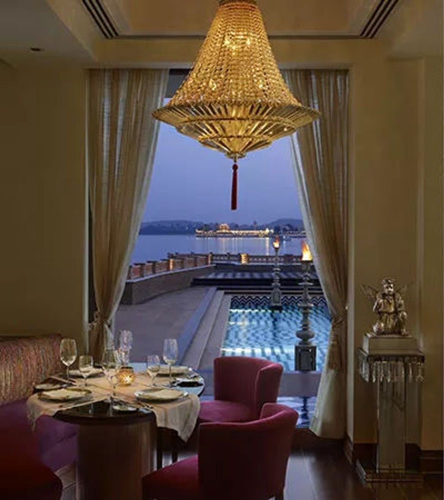 Majestic palace-style hotel on Lake Pichola with ornate domes and archways, illuminated at dusk against Udaipur's mountain backdrop