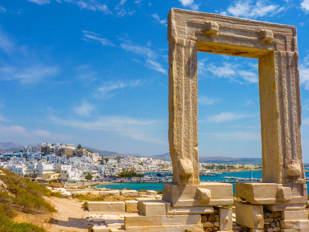 Traditional whitewashed Greek village with cubic houses cascading down hillside, overlooking crystal-clear Aegean Sea in Naxos