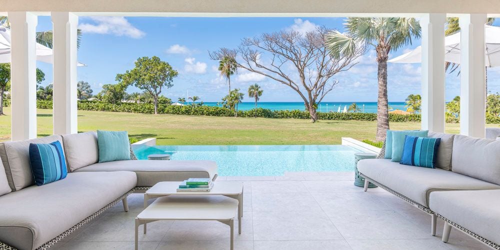 Spacious luxury family suite with ocean view, featuring elegant four-poster bed, white linens, and polished wooden furniture in a bright, airy Caribbean setting.