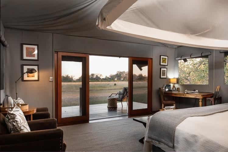 Luxurious safari tent suite at Chitabe Lediba Camp, featuring elegant wooden furnishings, crisp white linens, and expansive canvas windows overlooking Botswana's wilderness.