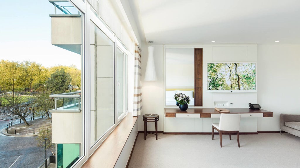Luxurious COMO Suite with plush white bedding, contemporary design, floor-to-ceiling windows overlooking urban London landscape, elegant neutral color palette
