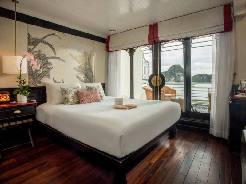 Elegant Long Quan Suite with panoramic windows, Vietnamese wooden furnishings, plush king bed, and sweeping views of scenic bay landscape aboard luxury cruise ship