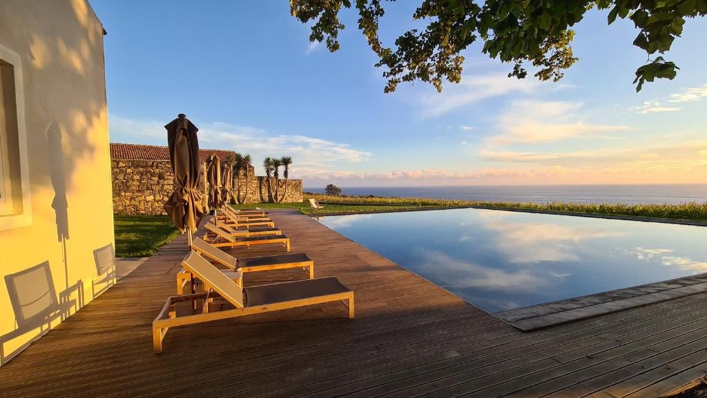 Elegant hotel nestled in lush Azorean landscape, featuring infinity pool overlooking ocean and volcanic mountains, white modern architecture