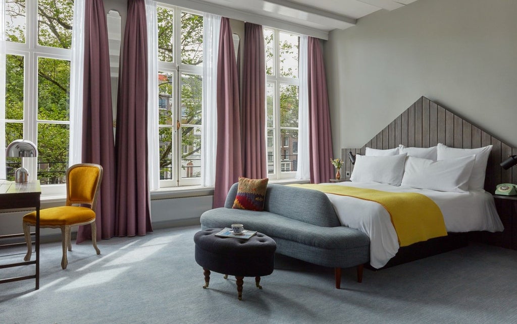 Elegant canal-view hotel room with herringbone wood floors, king bed, antique furnishings and large windows overlooking Amsterdam waterways