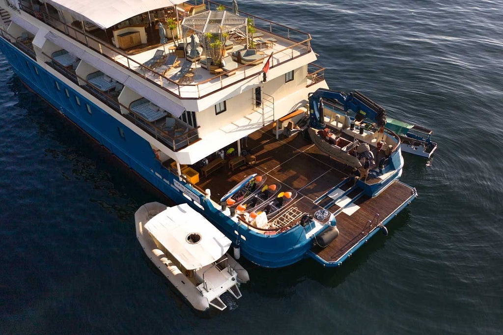 Luxurious expedition yacht Kudanil Explorer anchored in crystal-clear Indonesian waters, surrounded by lush tropical islands at sunset