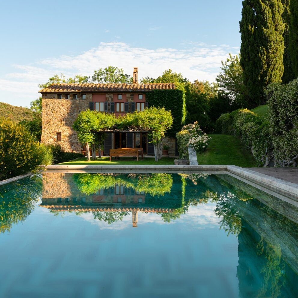 Luxurious stone Tuscan castle hotel with rustic stone walls, verdant rolling hills, and cypress trees in soft golden evening light