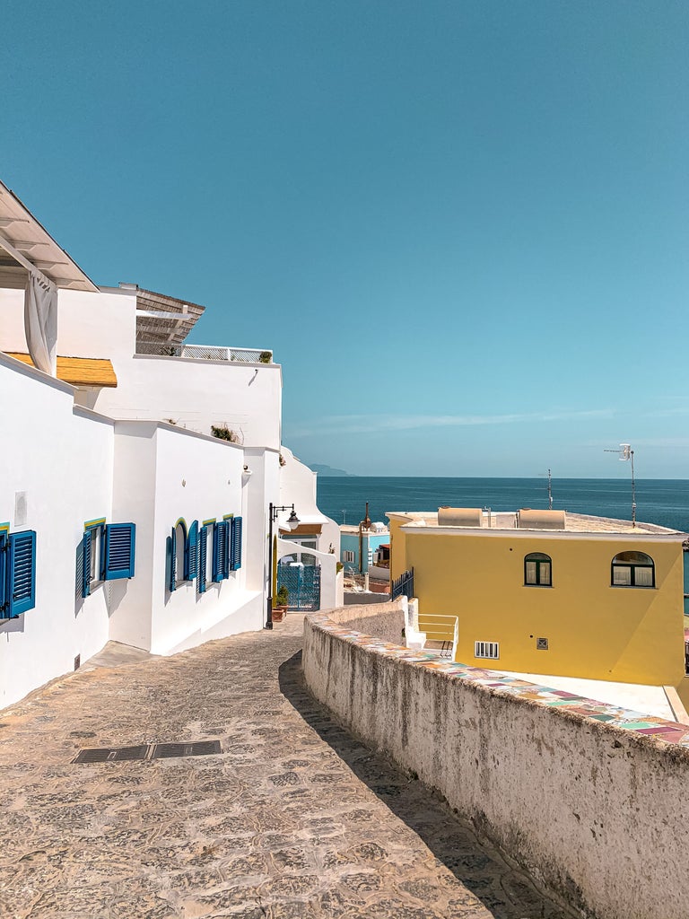 Sun-kissed Mediterranean villa perched on Ischia's coastal cliff, featuring elegant terraces with panoramic views of turquoise waters