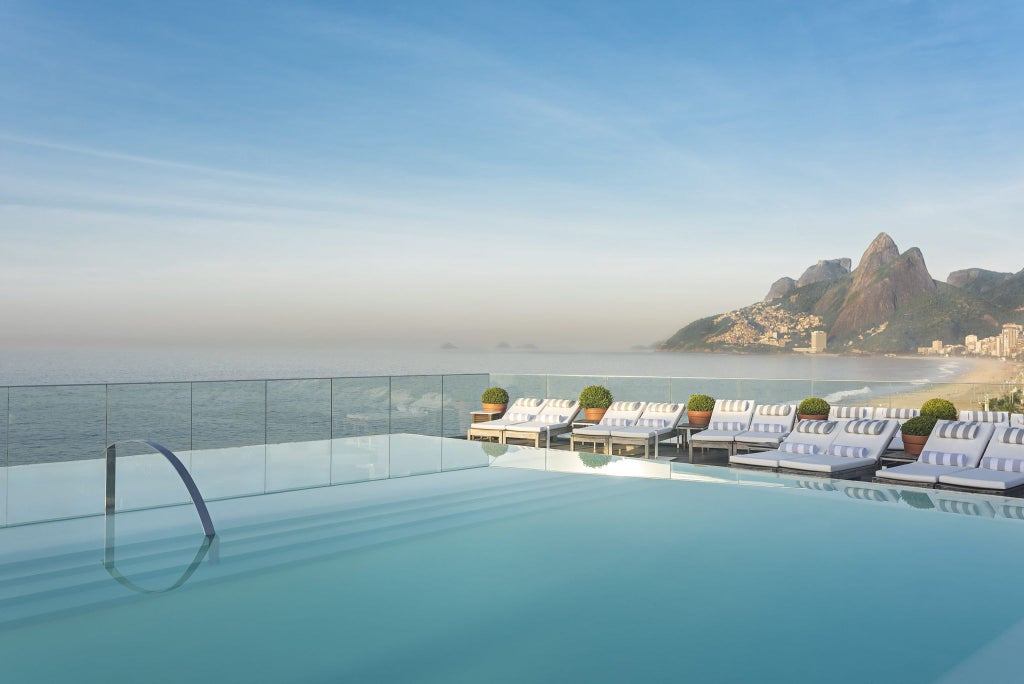 Luxurious Art Deco hotel overlooking Ipanema Beach, featuring elegant white facade, palm trees, and panoramic views of Rio's iconic coastline