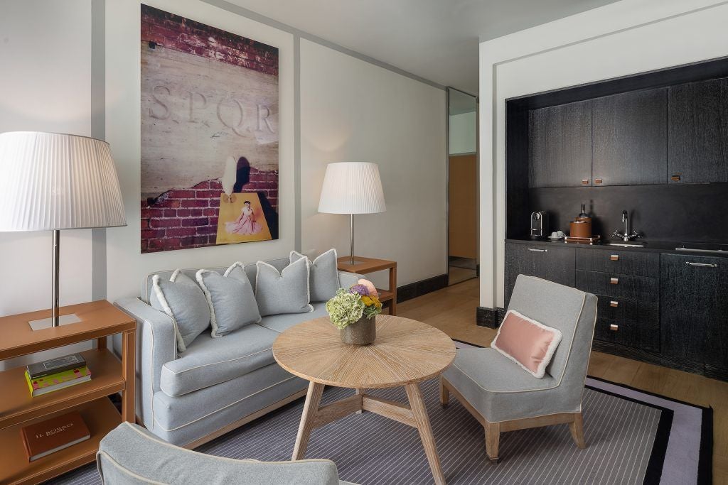 Elegant Roma hotel room with soft neutral tones, plush bedding, modern Italian design, and large windows overlooking city's historic architecture.