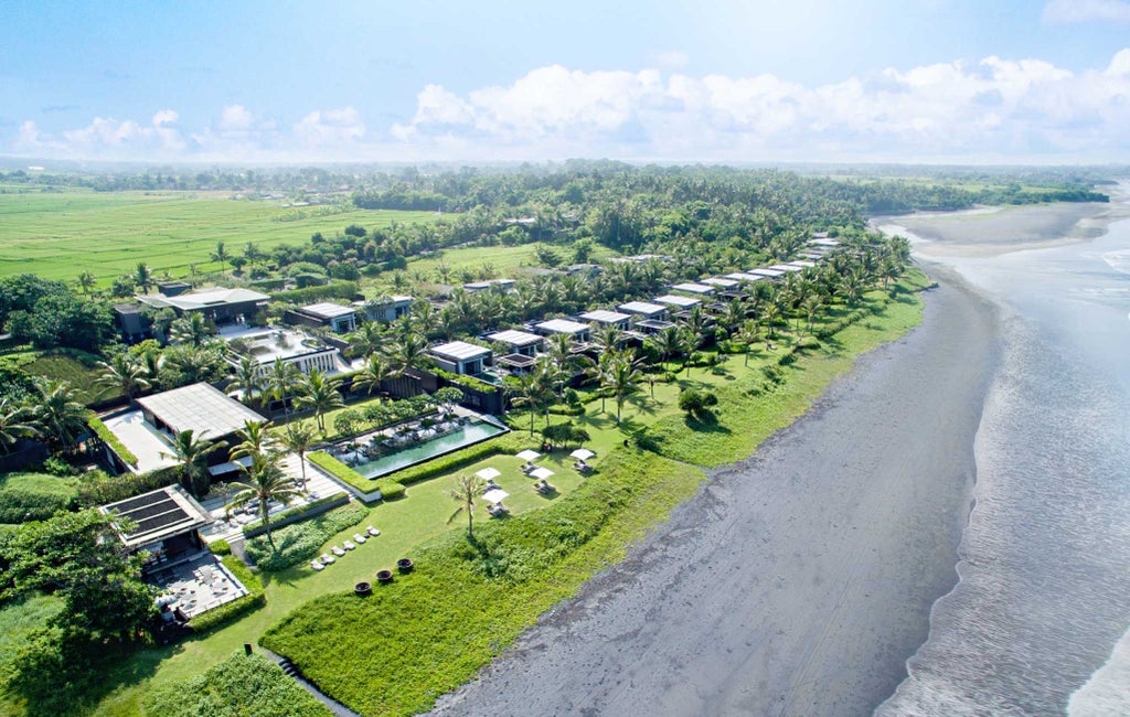 Infinity pool overlooking volcanic black sand beach at Soori Bali, with private oceanfront loungers and traditional Balinese architecture