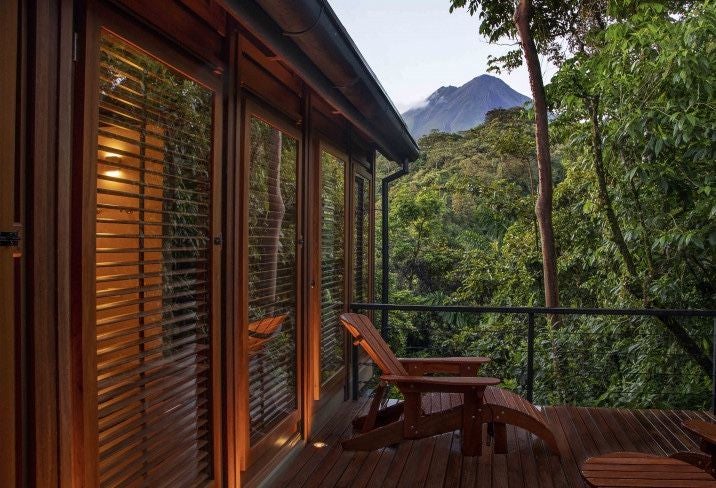 Contemporary luxury villa with floor-to-ceiling windows overlooking lush Costa Rican rainforest and Arenal Volcano, featuring infinity pool