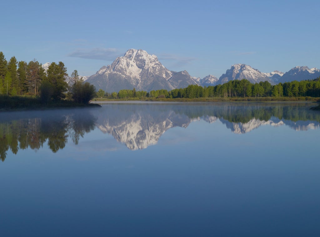 Luxurious mountain resort Amangani with infinity pool overlooking snow-capped Grand Tetons at golden sunset, wooden and stone facade