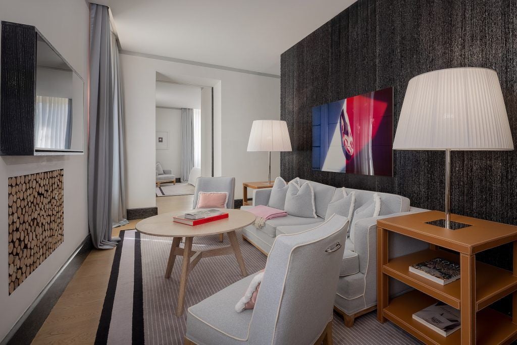 Luxurious hotel suite with marble floors, elegant cream furnishings, classic Italian design, and panoramic window overlooking scenset cityscape in Rome.