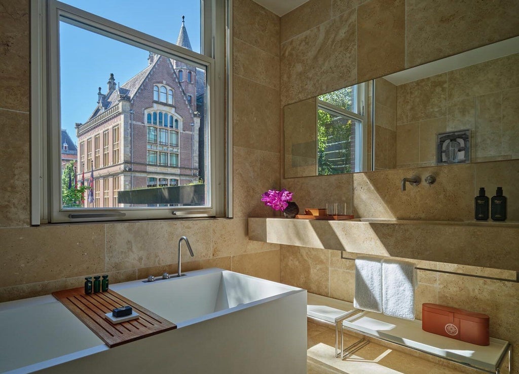 Luxurious garden-view one-bedroom suite at Conservatorium Hotel, Amsterdam, featuring modern design, plush furnishings, and expansive windows overlooking lush greenery.