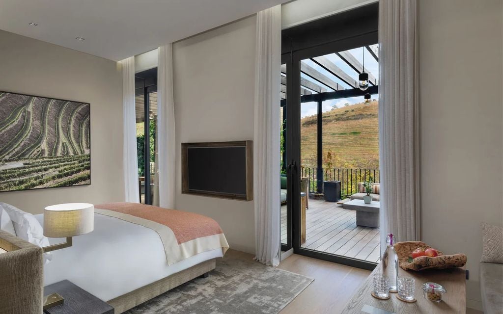 Elegant hotel suite with floor-to-ceiling windows overlooking Douro Valley vineyards, featuring modern furniture and natural wood accents