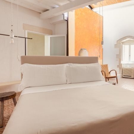 Elegant stone-walled boutique hotel room with rustic wooden furnishings, soft natural light, and minimalist Mediterranean design in Sicilian countryside