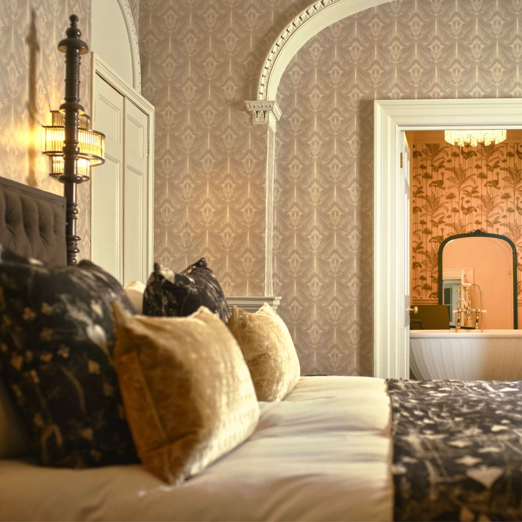 Elegant four-poster bed with luxurious cream linens in a spacious, refined suite at a boutique hotel, showcasing sophisticated British interior design