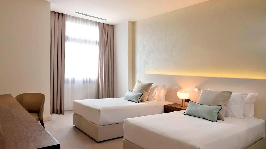 Elegant twin hotel room with lagoon views, featuring cream walls, plush beds, modern lighting, and upscale contemporary furnishings.