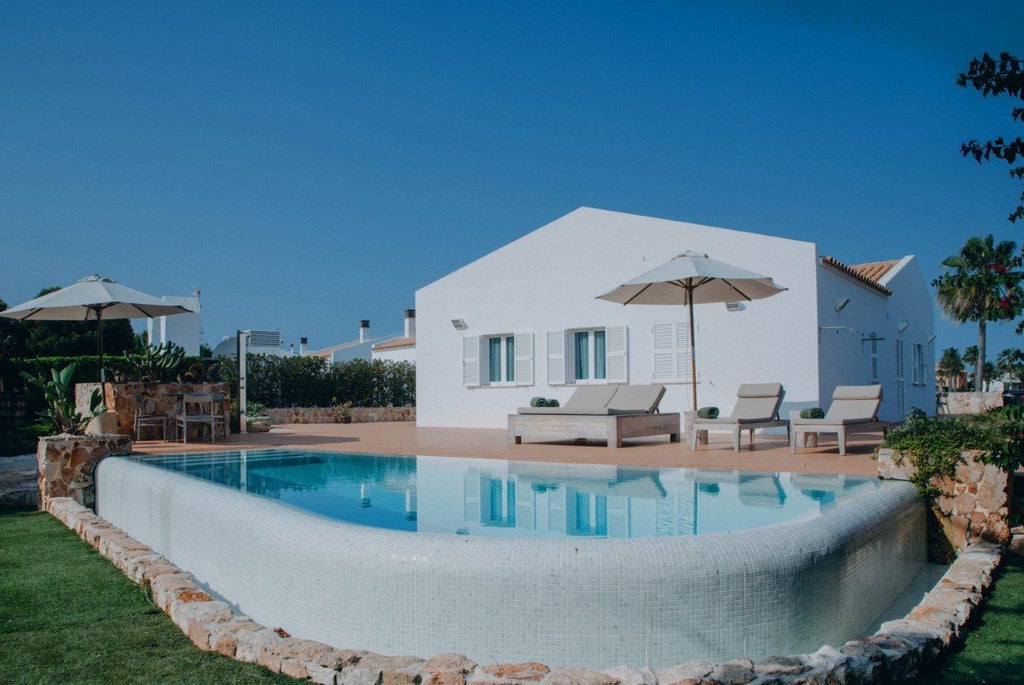 Luxurious white-washed Mediterranean resort with azure pool, lush palm trees, and traditional Spanish architecture overlooking scenic Menorca coastline