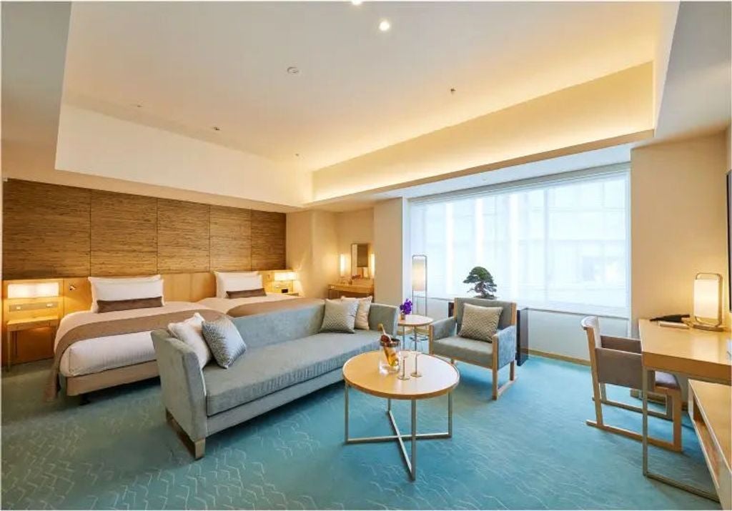 Modern Japanese hotel suite with luxurious king bed, city views through floor-to-ceiling windows, elegant seating area, and minimalist decor