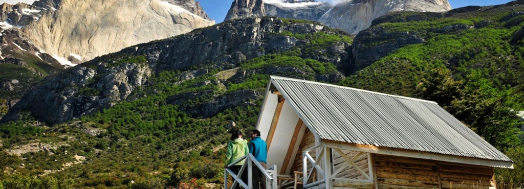 Luxurious mountain cabin with large windows overlooking rugged Patagonian peaks, warm wooden interior, and elegant rustic design at Hotel Las Torres