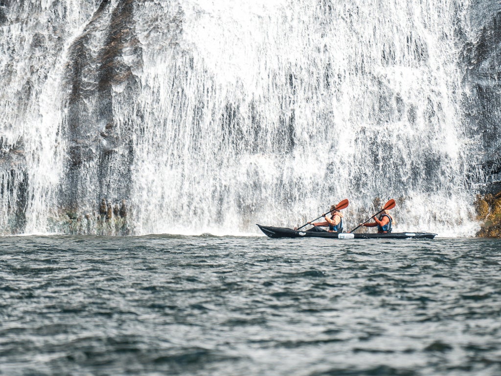 Serene fjord landscape with kayaker gliding through crystal-clear waters, surrounded by steep cliffs and lush greenery in pristine Norwegian wilderness