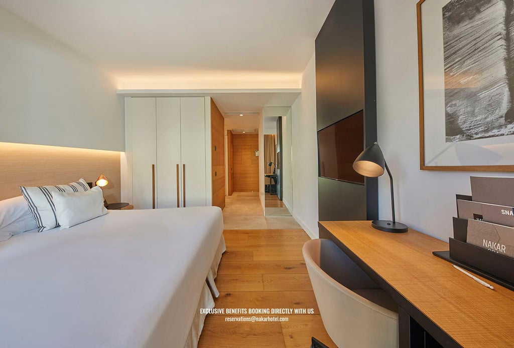 Elegant superior hotel room with plush white bedding, contemporary design, and a private balcony overlooking urban scenery in a Spanish boutique hotel