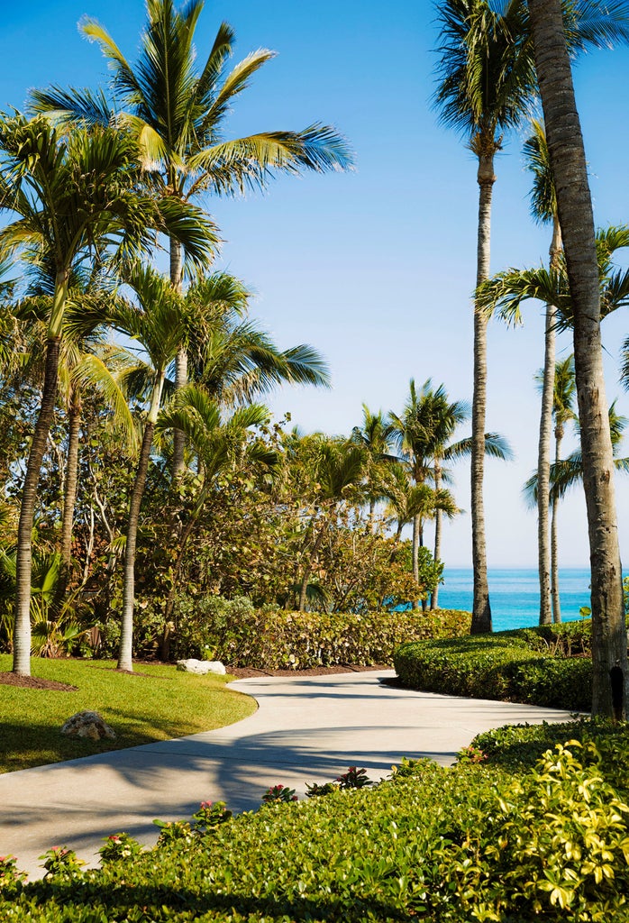 Oceanfront luxury resort with white sand beach, multiple infinity pools, swaying palm trees and elegant beachside cabanas at sunset